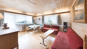 Una habitación acogedora con techo de madera, un comedor con mesa y sillas, un sofá rojo y un televisor sobre una mesita auxiliar.