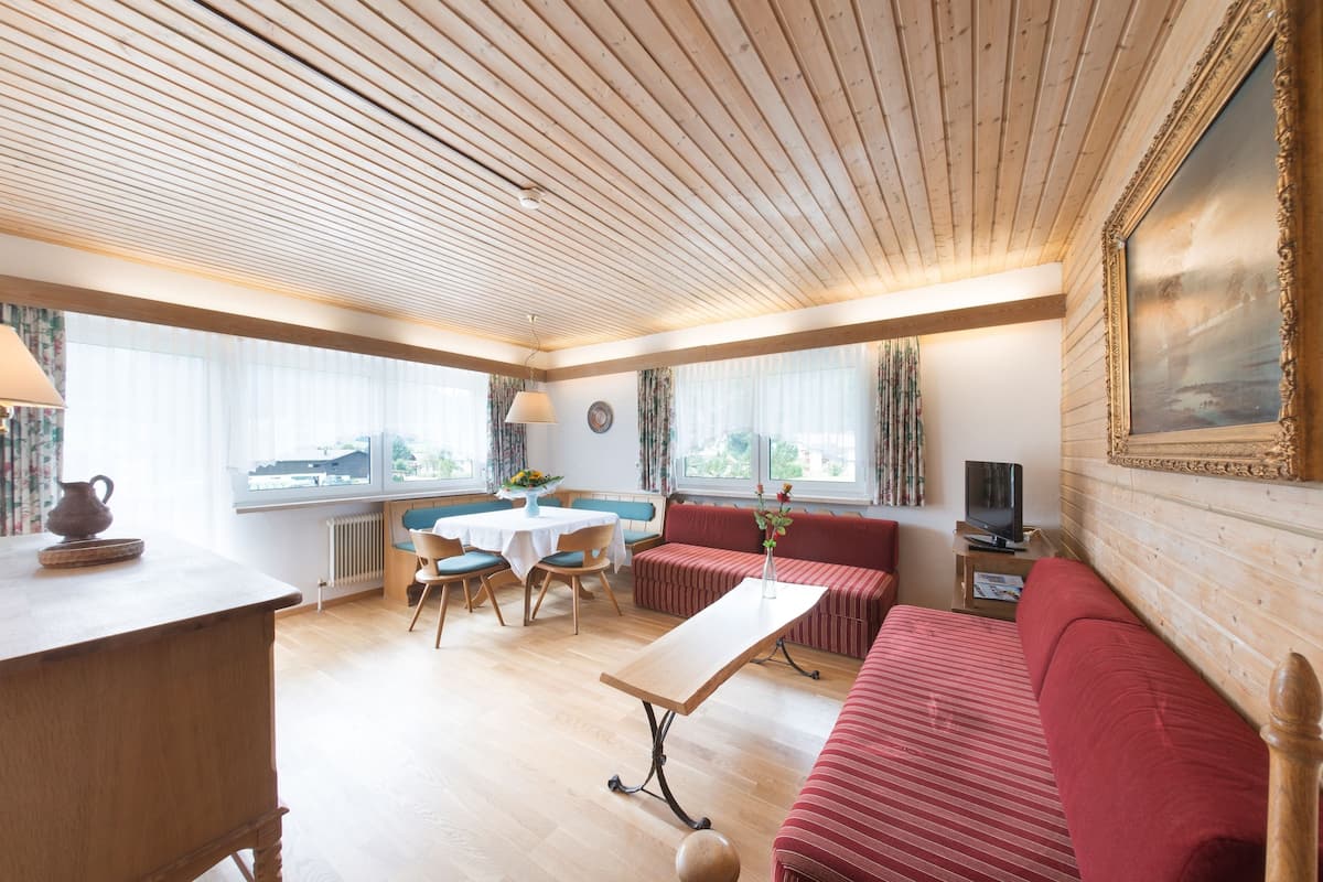 Une pièce chaleureuse avec un plafond en bois, un coin repas comprenant une table et des chaises, un canapé rouge et un téléviseur posé sur une table d’appoint.