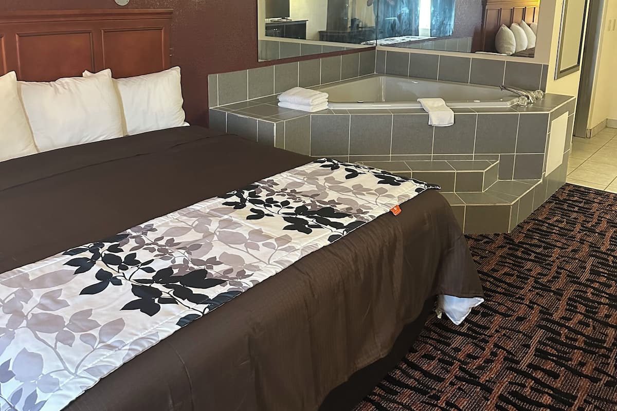 A hotel room with a large bed, a bathroom with a bathtub, and a mirror reflecting the room.