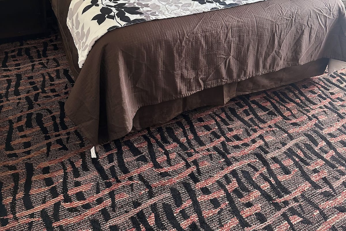 A hotel room with a large bed, green walls, a patterned carpet, and bedside lamps.
