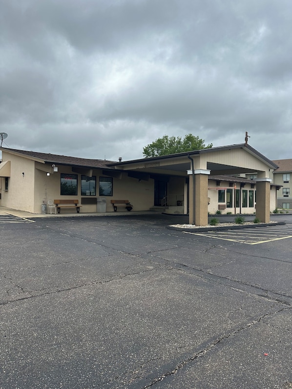 A building with a covered entrance, a bench, and a parking lot.
