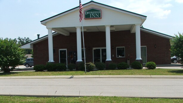 A brick building with a white facade, columns, and a sign reading "Deerfield Inn." - Deerfield Inn & Suites (Greenbrier)