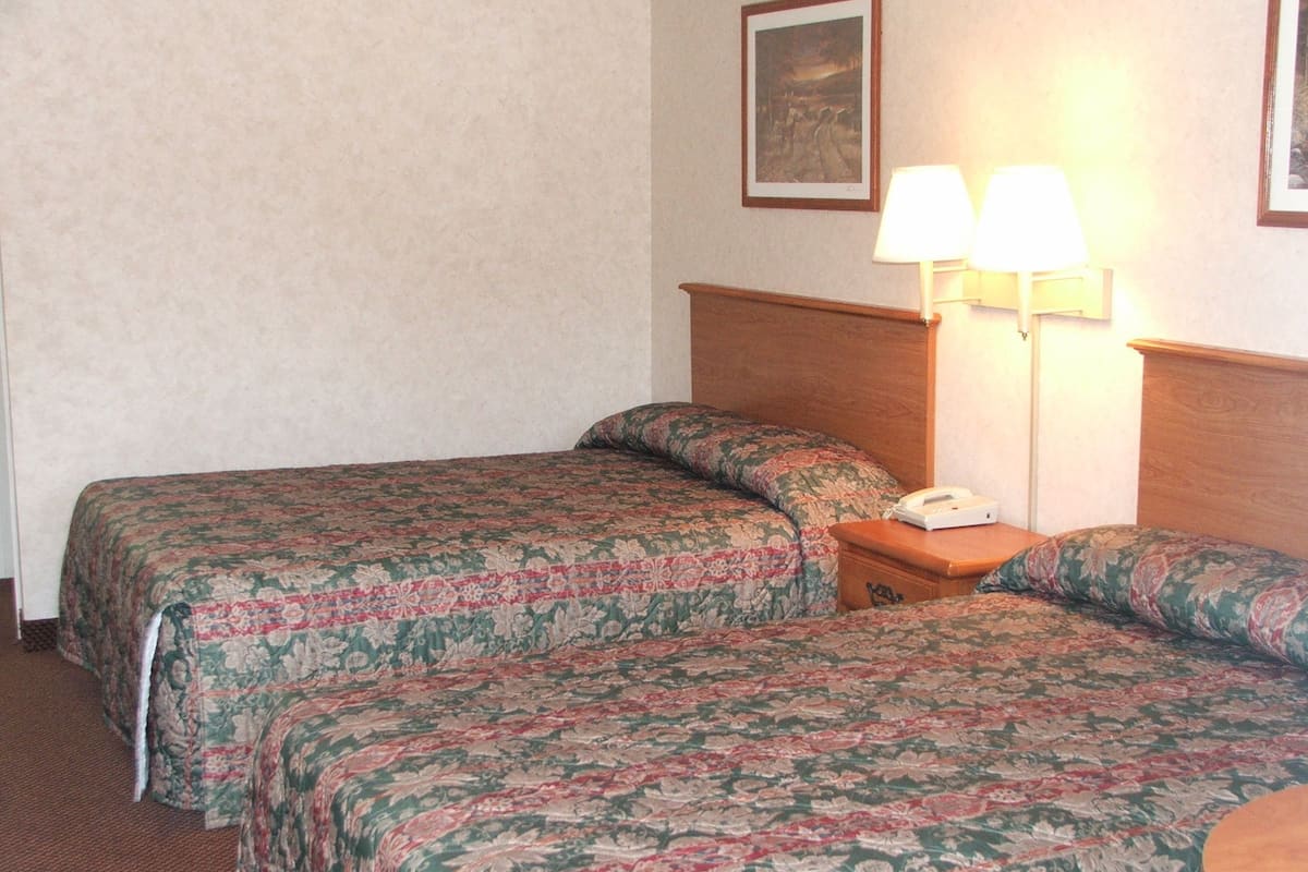 Habitación de hotel con dos camas, cada una con ropa de cama de motivos florales, una mesita de noche con lámpara y teléfono.
