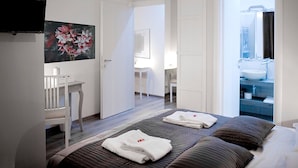 Une chambre d’hôtel avec un lit, un bureau, un tableau et une salle de bain visible à travers une porte ouverte.