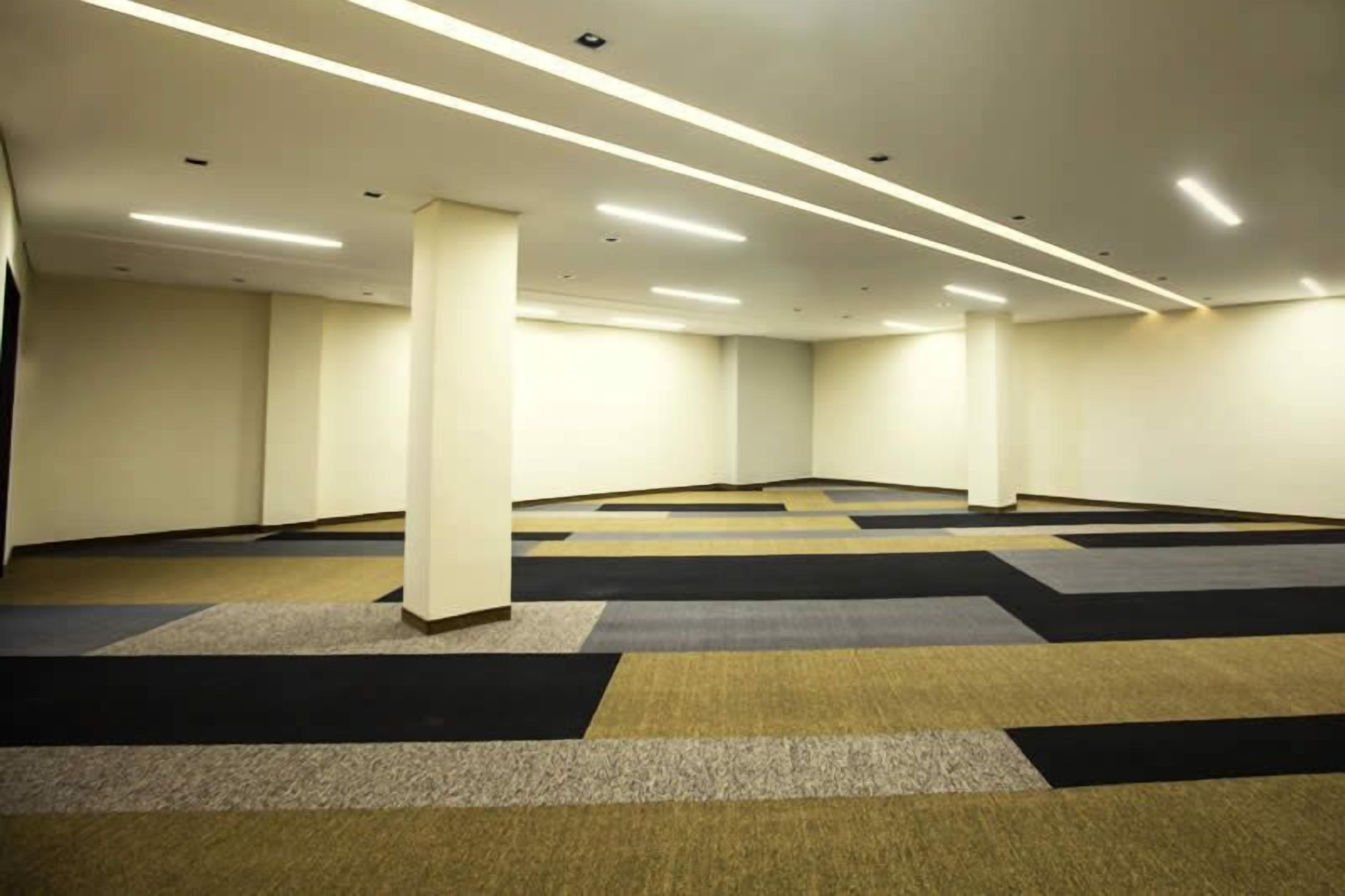 A spacious, well-lit room with a modern design, featuring a carpeted floor and a high ceiling with recessed lighting.