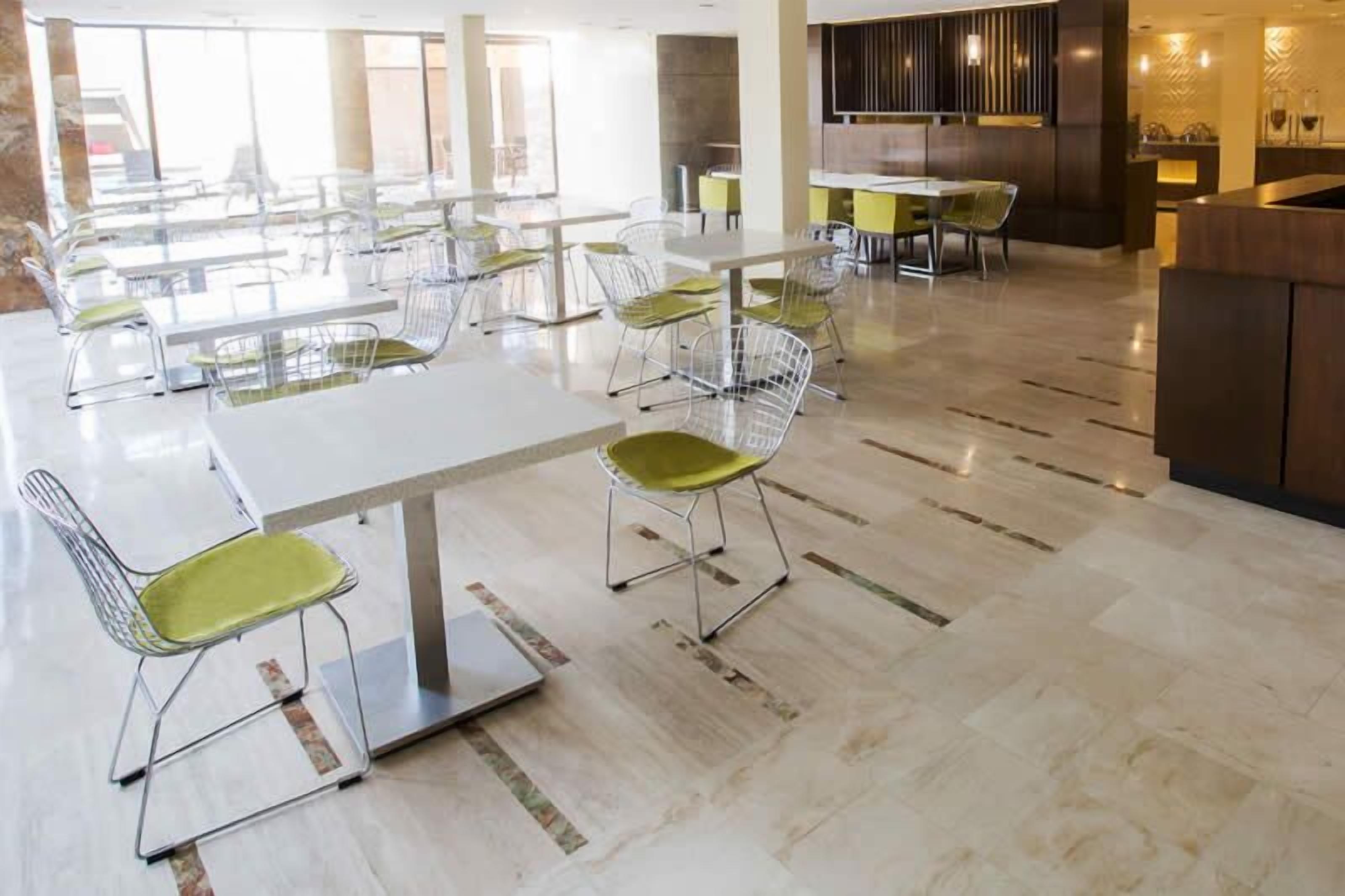 A spacious dining area with multiple tables and chairs, a modern kitchen area, and a view of the outdoors.
