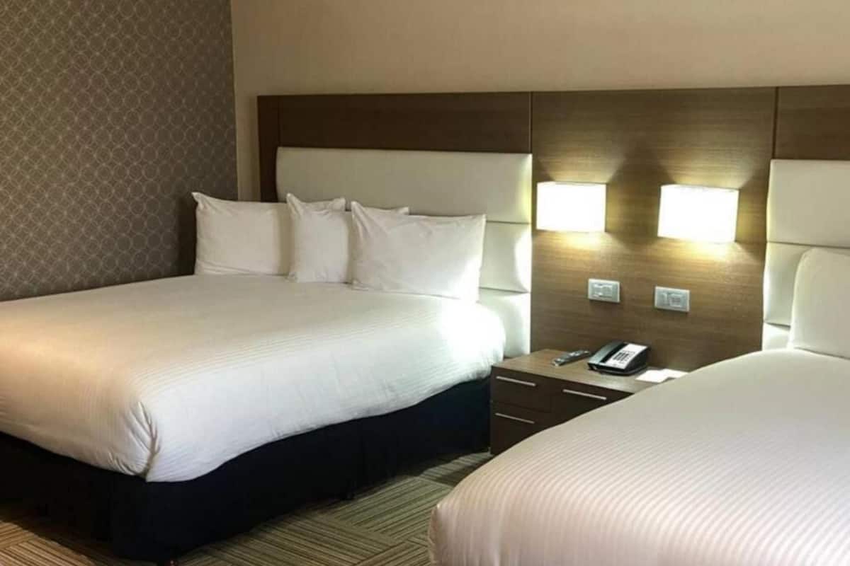 Una habitación de hotel con una cama grande, una mesita de noche con teléfono y dos lámparas de pared.