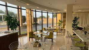 Un comedor moderno con divisiones de vidrio, sillas acolchadas verdes y vistas al exterior.