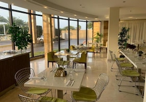 Un comedor moderno con divisiones de vidrio, sillas acolchadas verdes y vistas al exterior.