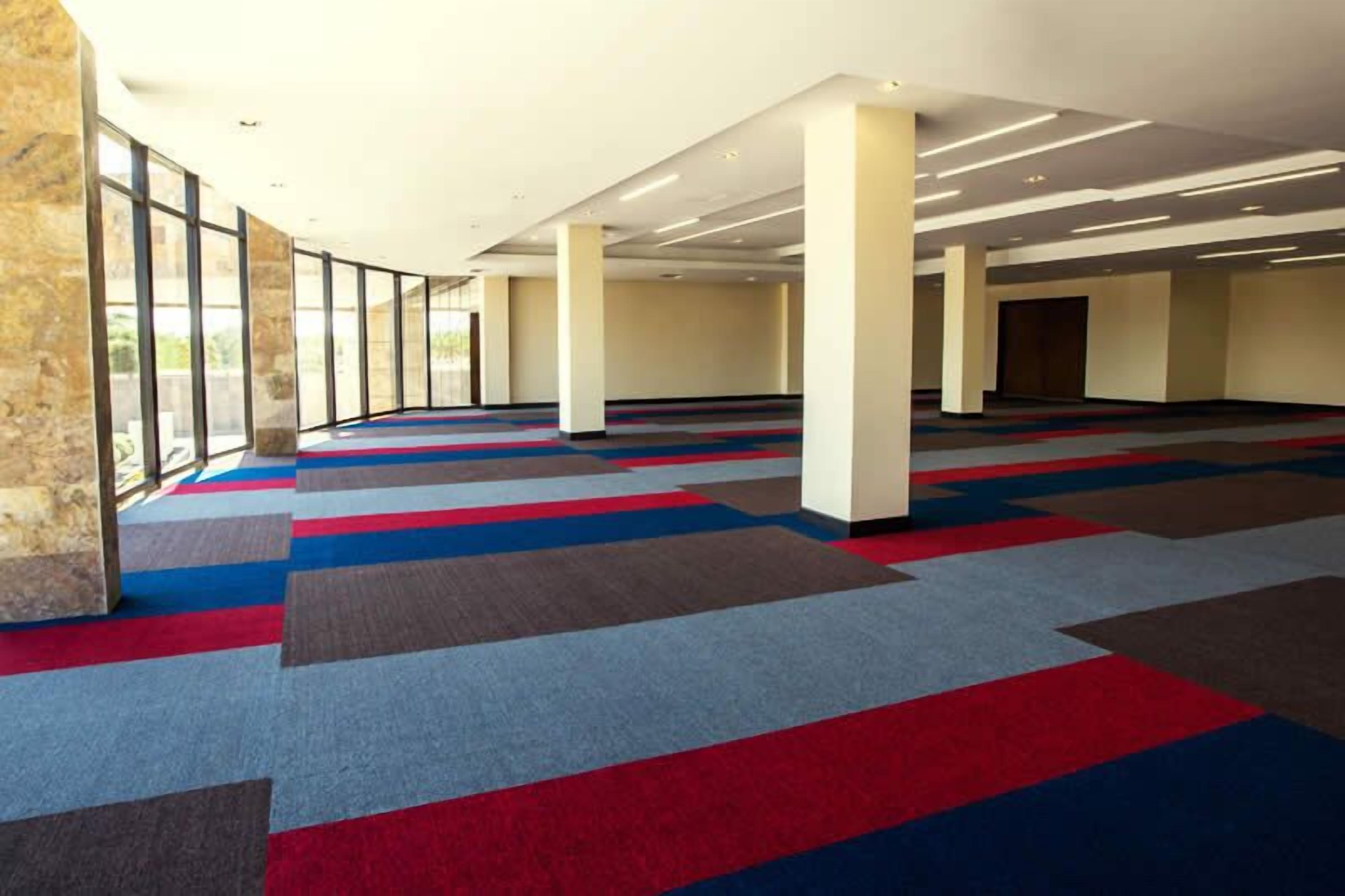 A spacious indoor area with a patterned carpet, large windows, and a high ceiling.