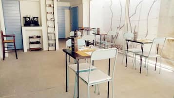 Uma sala de jantar com mesas e cadeiras, uma máquina de café e uma estante com diversos objetos.