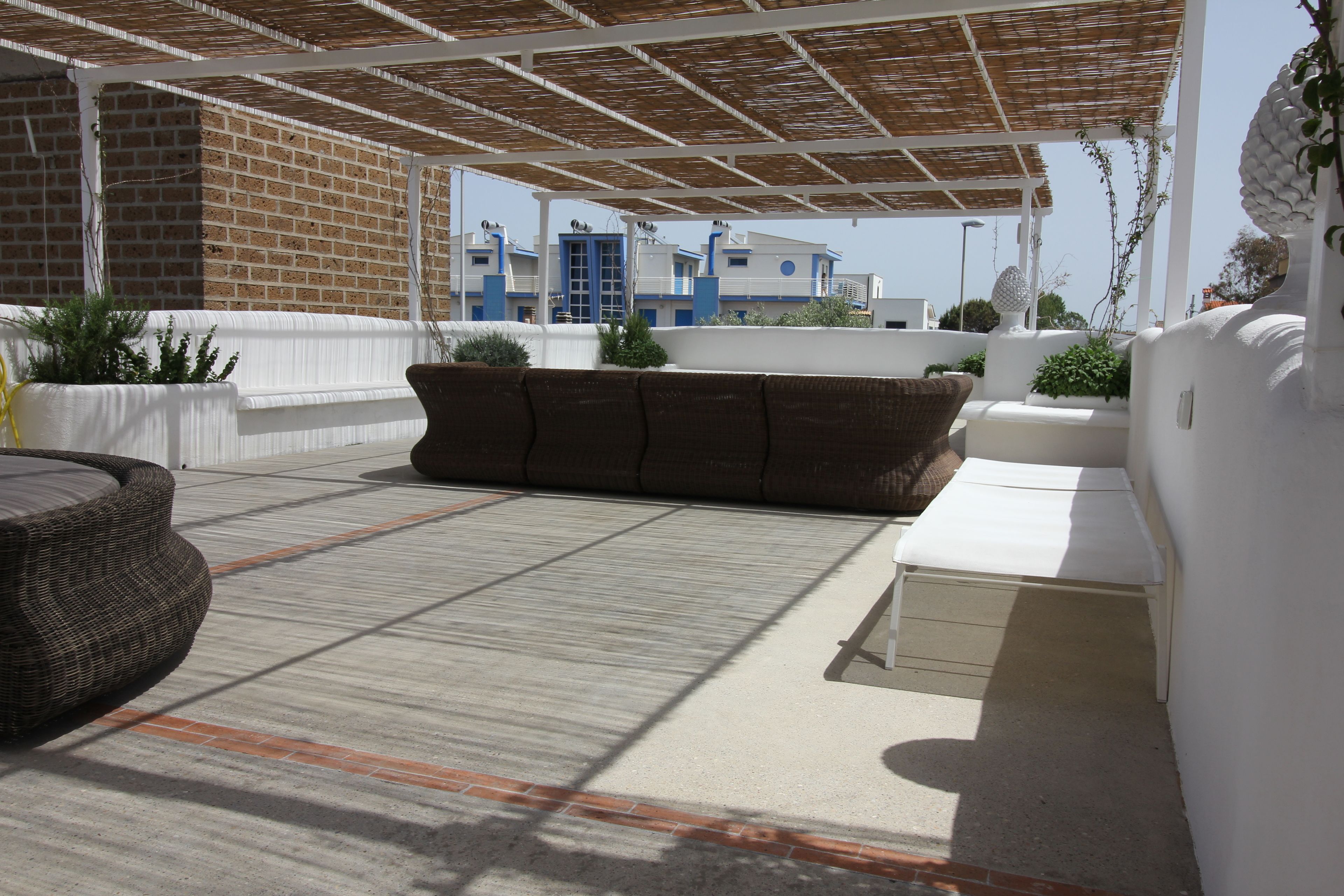 Een overdekt terras met een betonnen vloer, een bruine bank en een witte zitbank.
