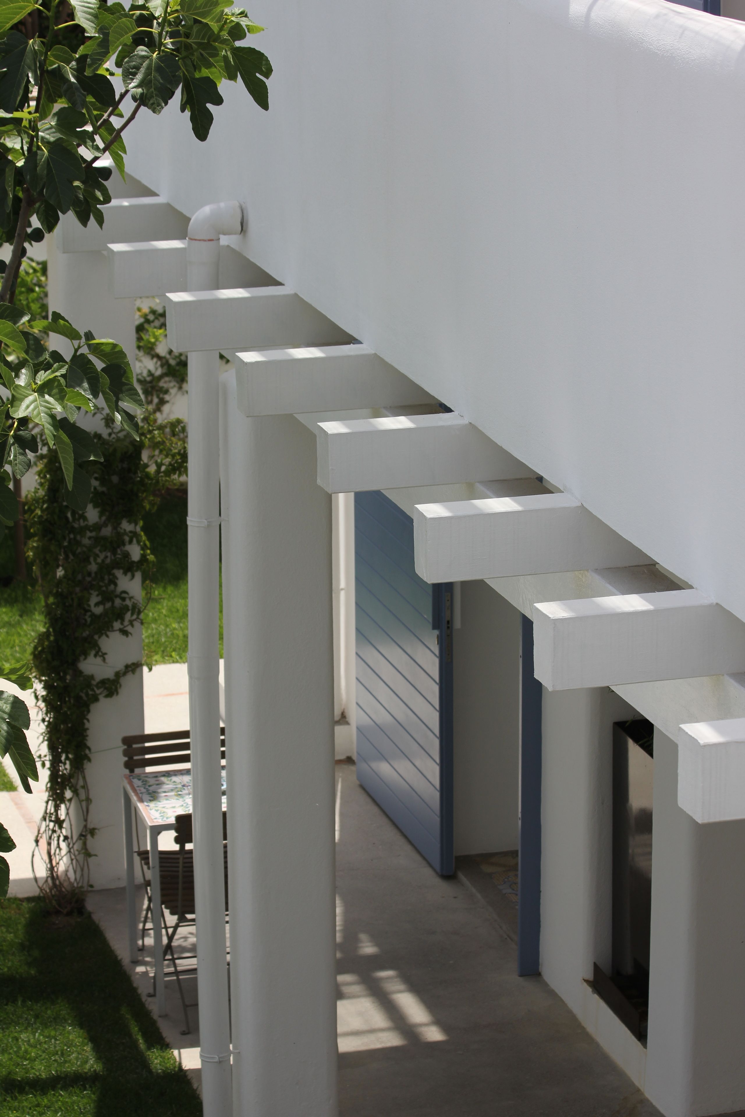 Een modern buitengebied met een witte constructie, een tafel en stoelen, omringd door groen.