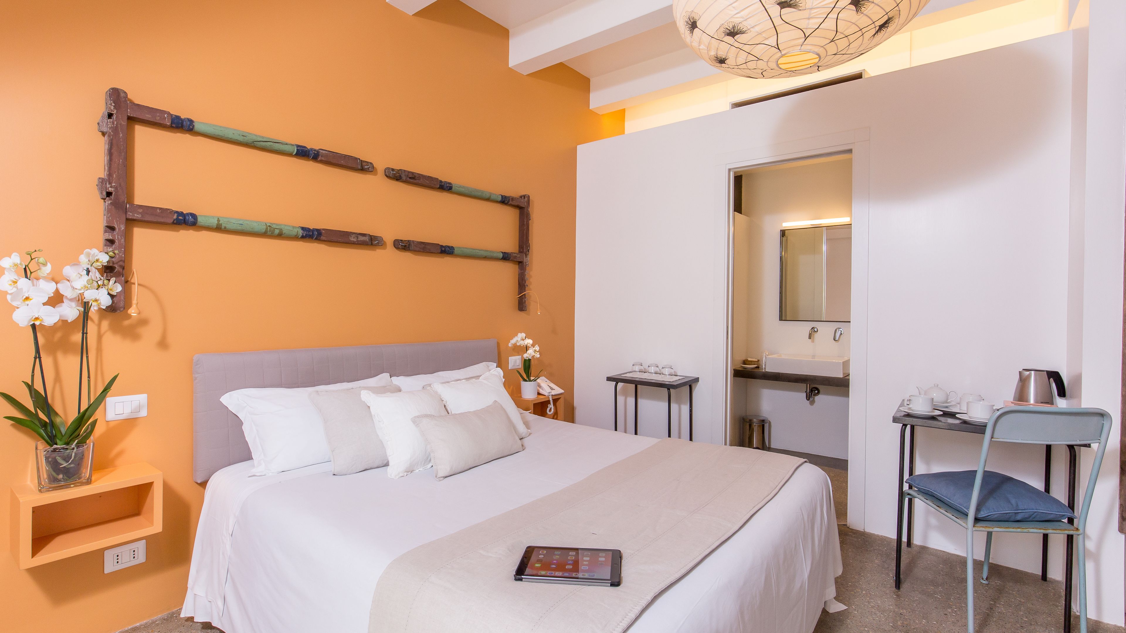 A neatly arranged hotel room with a bed, bedside table, chair, and a small table with a lamp.