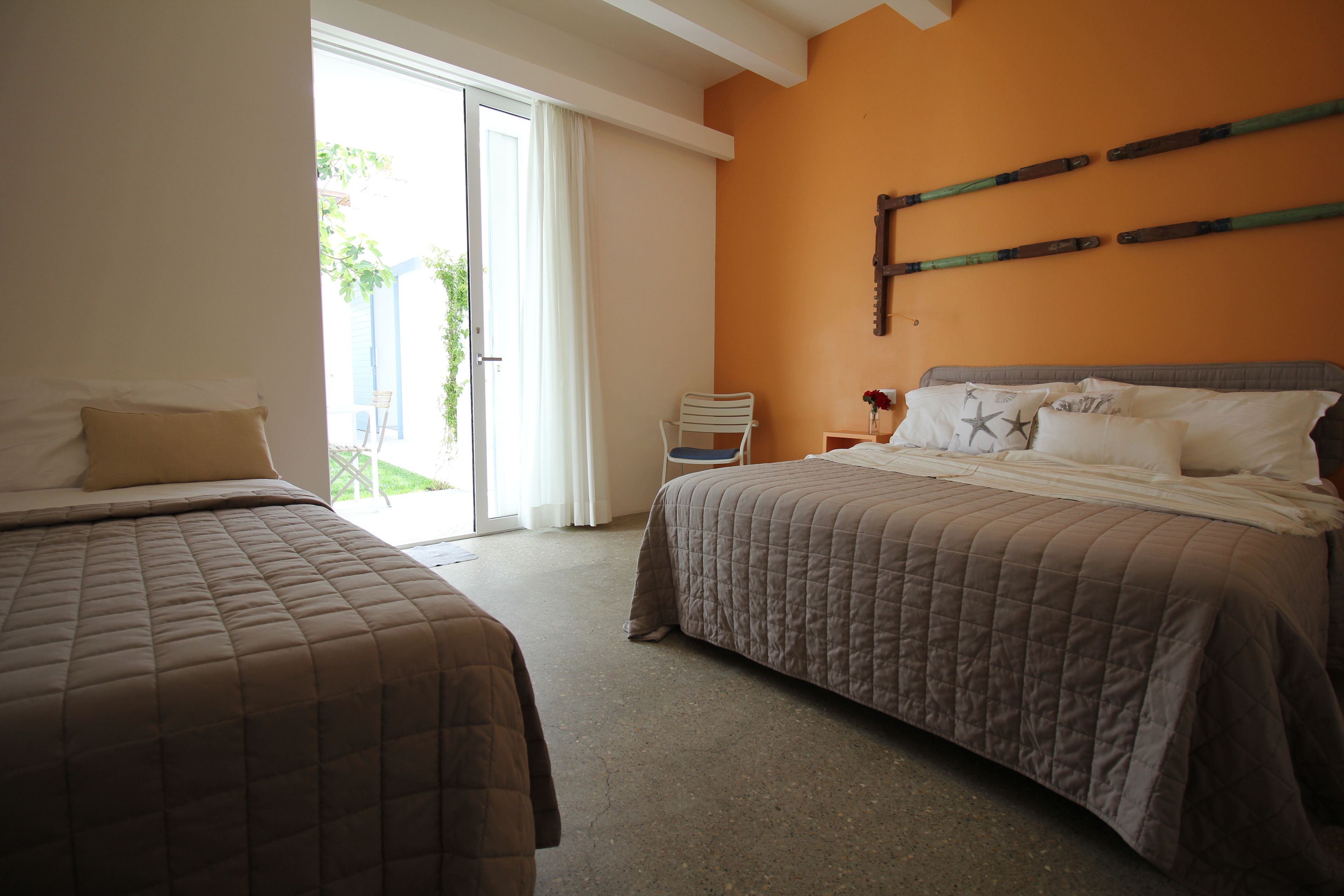 Quarto de hotel com duas camas, porta de vidro deslizante para o exterior e decoração de madeira fixada na parede.