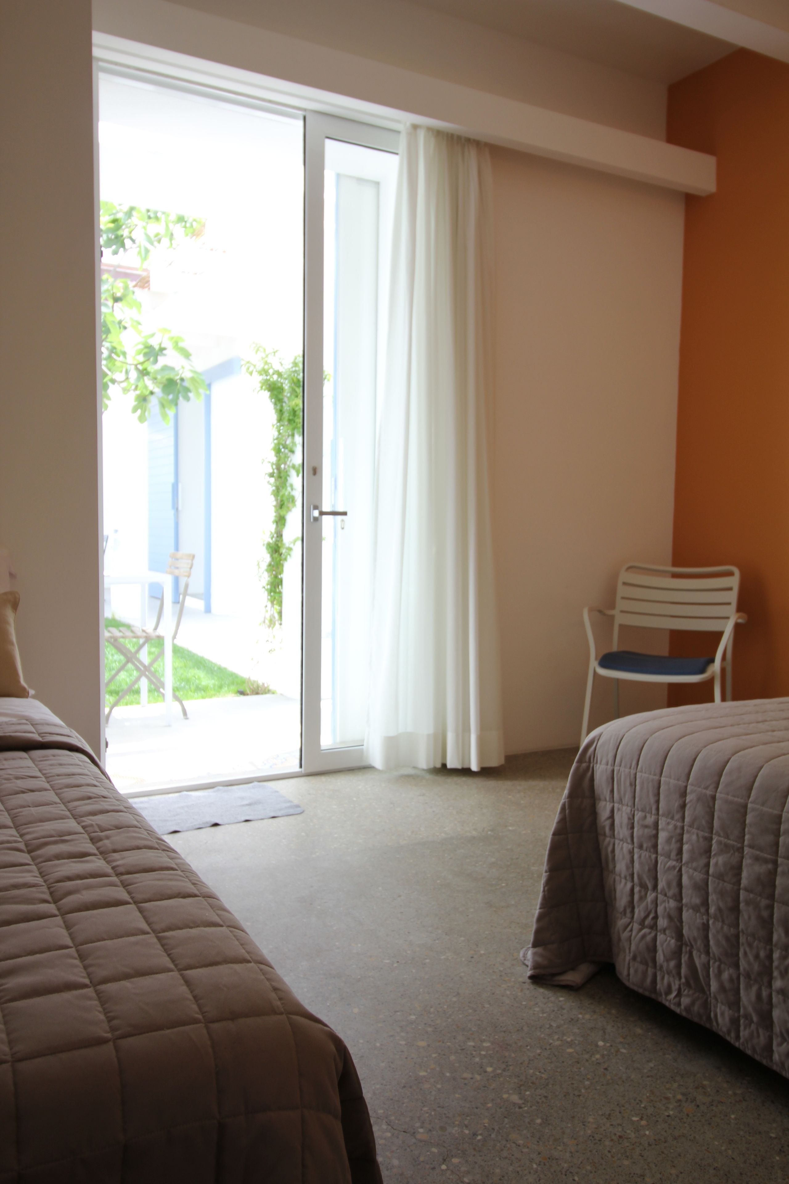 Een hotelkamer met twee bedden, een schuifdeur naar buiten, een stoel en een klein tafeltje.