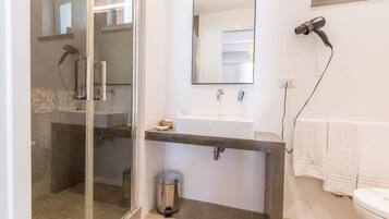 A bathroom with a glass shower enclosure, a white sink, a towel rack, and a hairdryer on the wall.