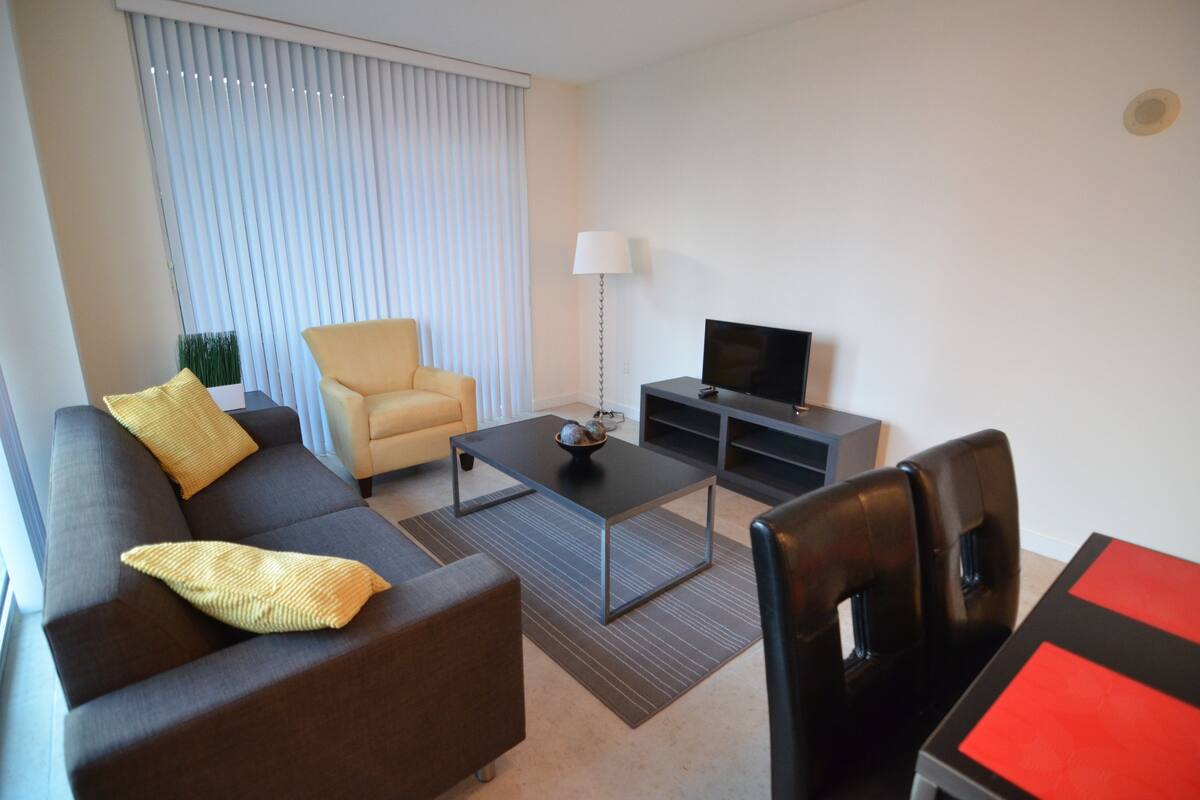 Una sala de estar moderna con sofá, sillón, mesa de centro, mueble para televisión y una mesa de comedor.