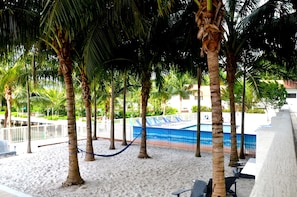 A sandy beach area with palm trees and a pool. - Riviera Luxury Living at River Oaks Marina and Tower (Miami)