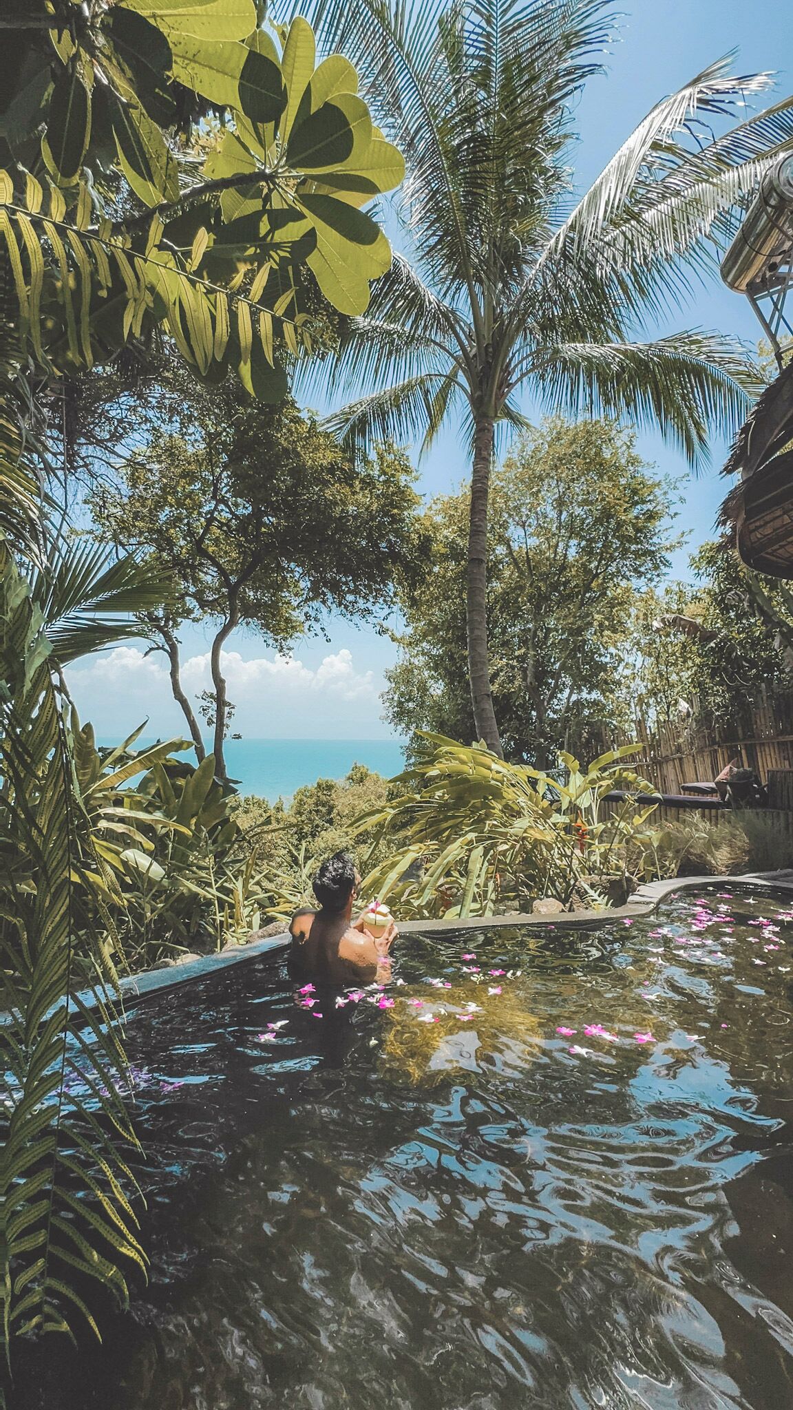 Una persona en una piscina natural rodeada de vegetación tropical y vista al mar.