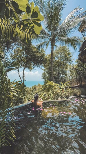 Una persona en una piscina natural rodeada de vegetación tropical y vista al mar.