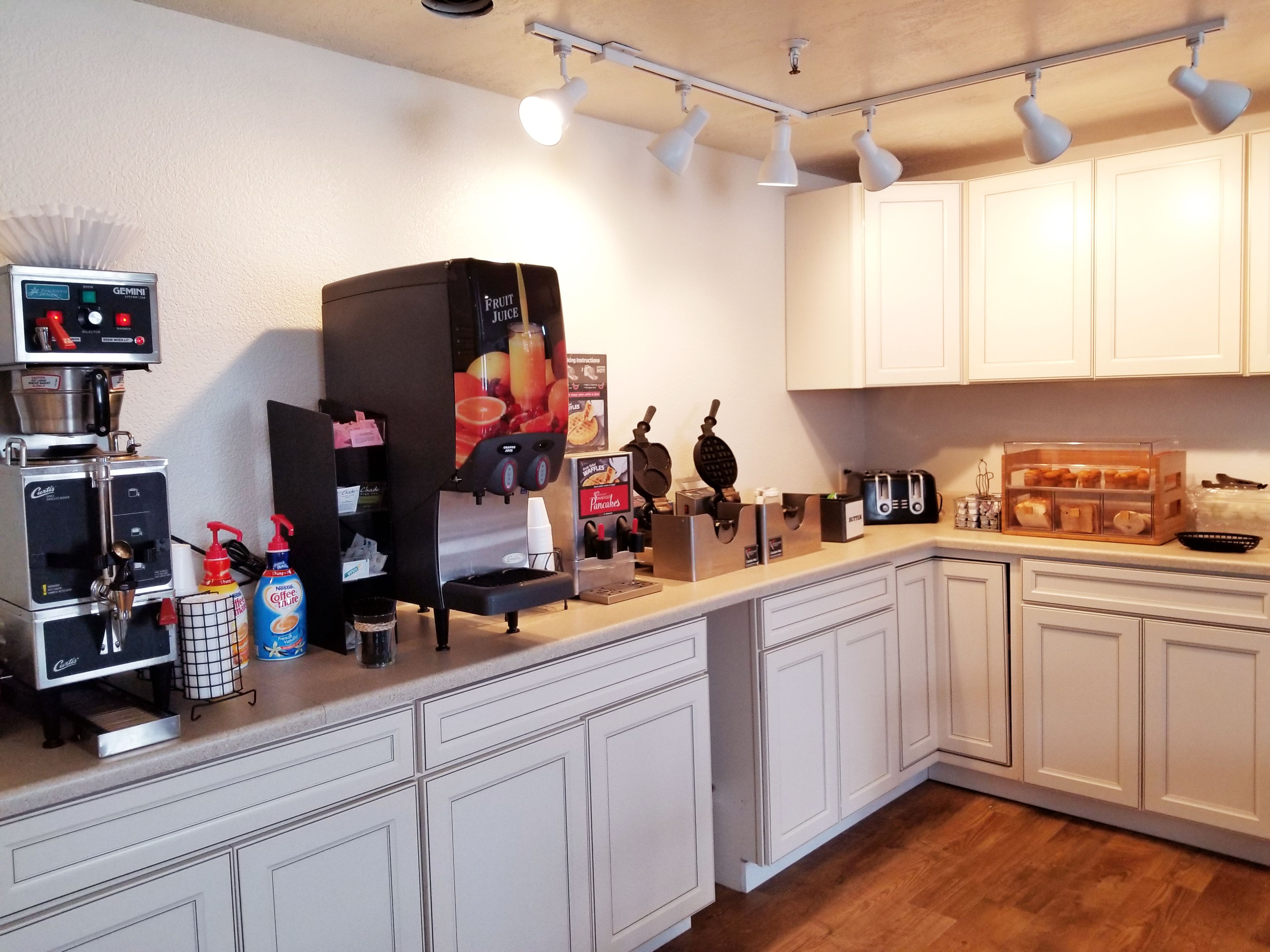 A kitchen with a coffee machine, a fruit juice dispenser, a waffle maker, and a toaster.