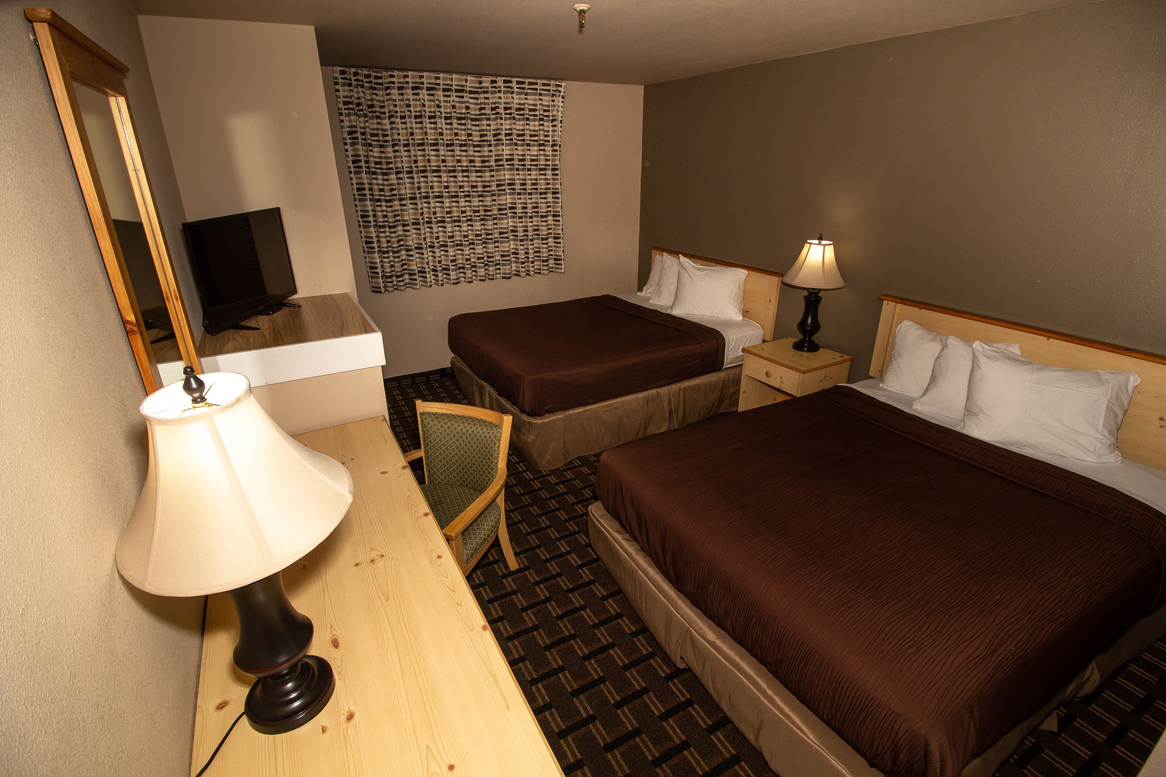 Une chambre d’hôtel avec deux lits, un bureau avec une lampe, une chaise, un téléviseur et une décoration murale à motifs.