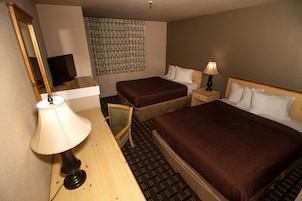 A hotel room with two beds, a desk with a lamp, a chair, a television, and a patterned wall hanging.