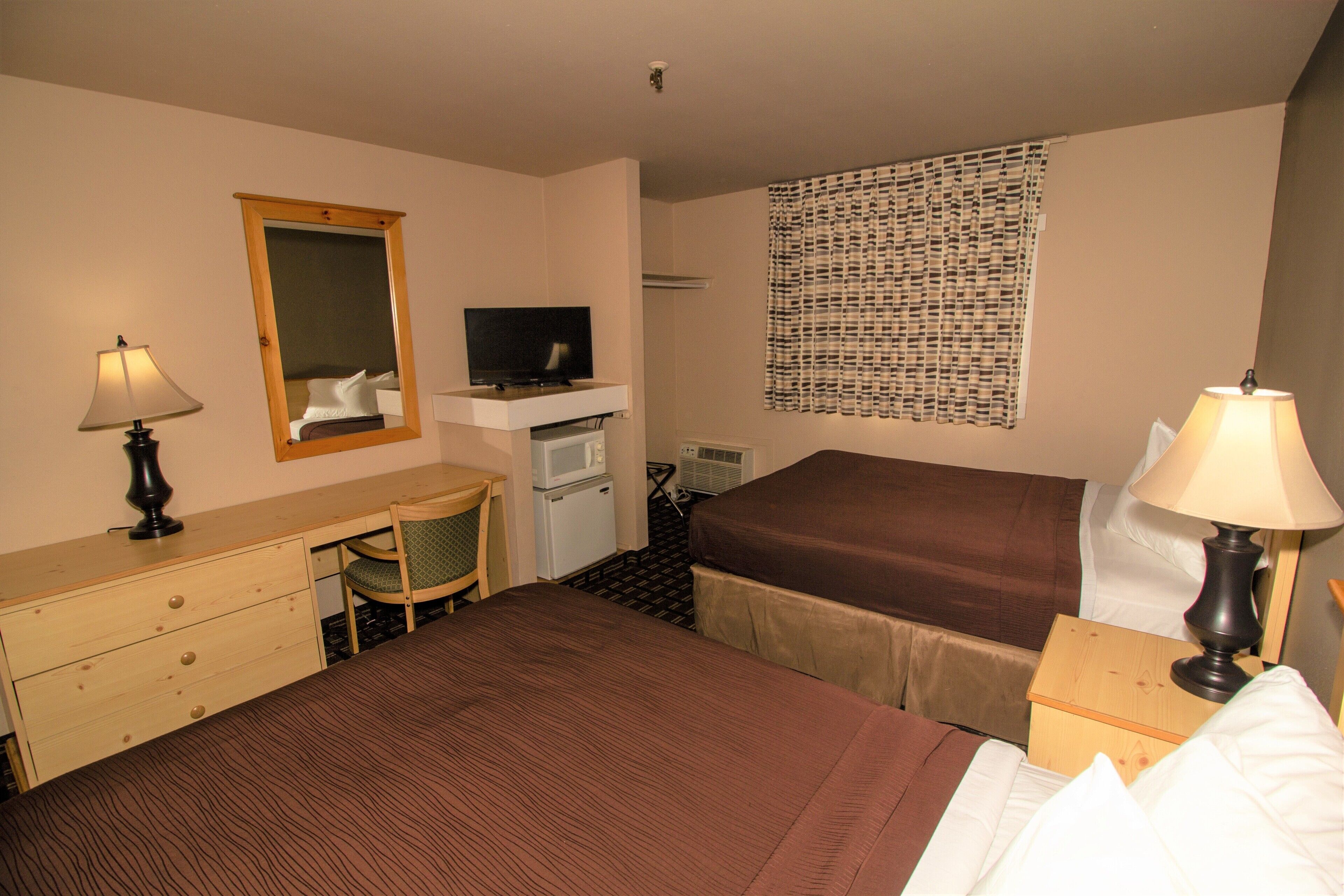 Habitación de hotel con cama, escritorio con silla, televisor, microondas y ventana con cortinas estampadas.