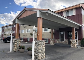 A hotel entrance with a covered walkway, stone pillars, and potted plants.