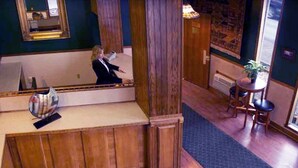 A hotel lobby with a wooden reception desk, a mirror, and a seating area with chairs and a table. - FairBridge Inn - Coeur d'Alene (Coeur d'Alene)