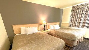 A hotel room with two beds, a nightstand with a lamp, a window with blinds, and a patterned carpet. - FairBridge Inn - Coeur d'Alene (Coeur d'Alene)