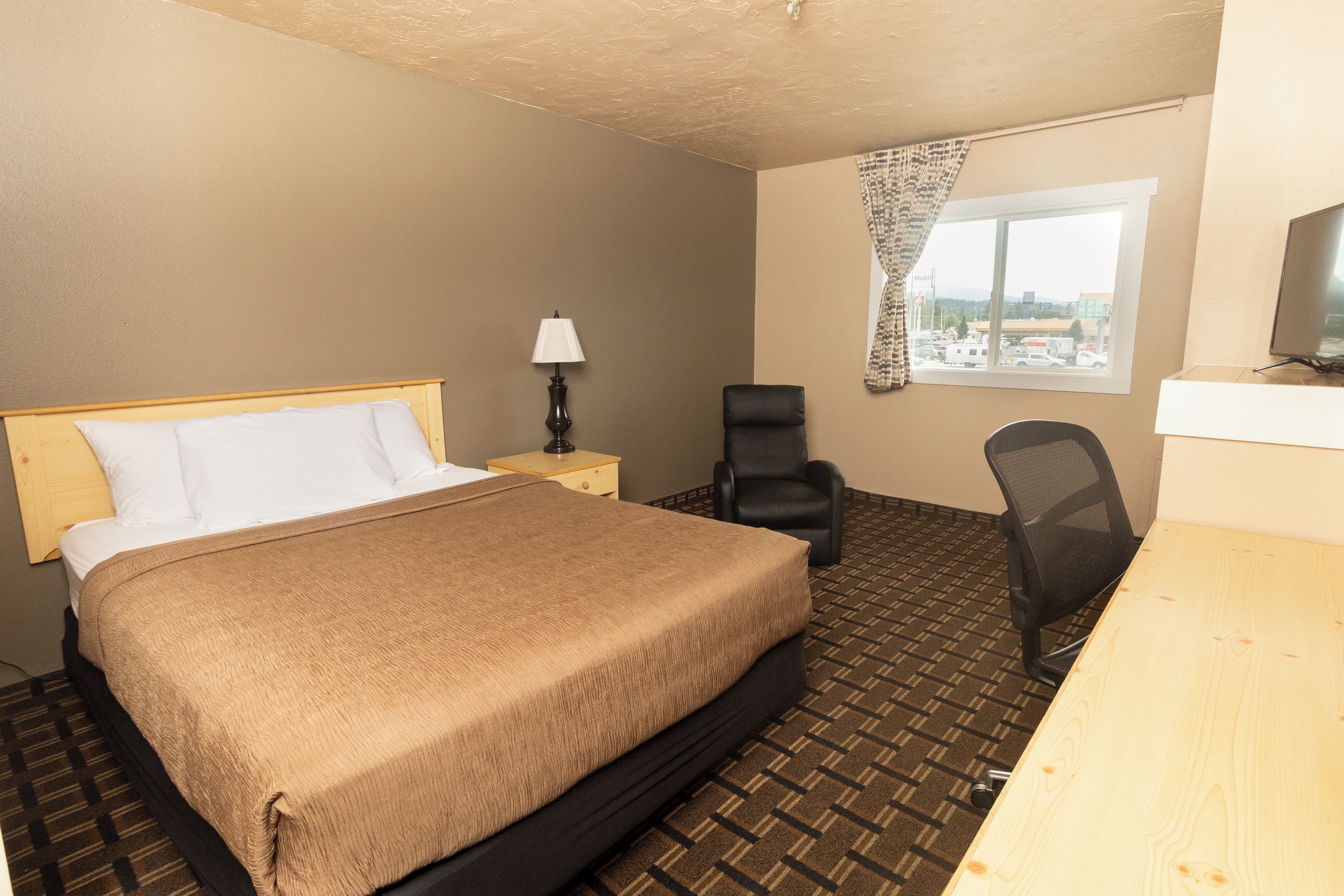 A hotel room with a bed, a desk, a chair, a lamp, and a window with a view of the outside.