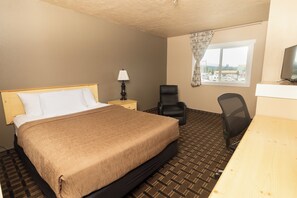 A hotel room with a bed, a desk, a chair, a lamp, and a window with a view of the outside.
