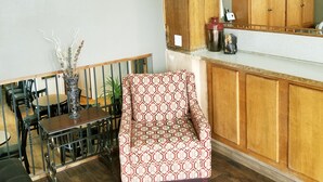 A dining area with a wooden table, chairs, and a patterned armchair. A clock and potted plants are on the wall. - FairBridge Inn - Coeur d'Alene (Coeur d'Alene)