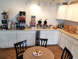 A kitchen with white cabinets, a coffee machine, waffle maker, and a fruit juice dispenser.