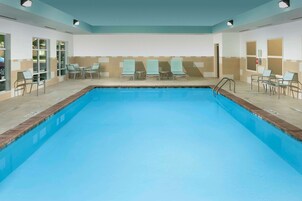A swimming pool with lounge chairs and tables, surrounded by walls with windows and doors.