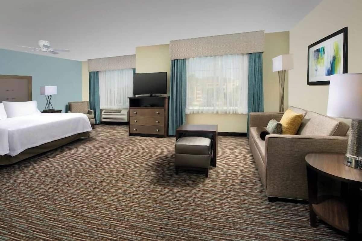 Une chambre d’hôtel avec un lit, un canapé, une petite table, une télévision et une fenêtre avec des rideaux.