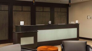 A reception area with a dark reception desk, two grey chairs, and a wooden table.