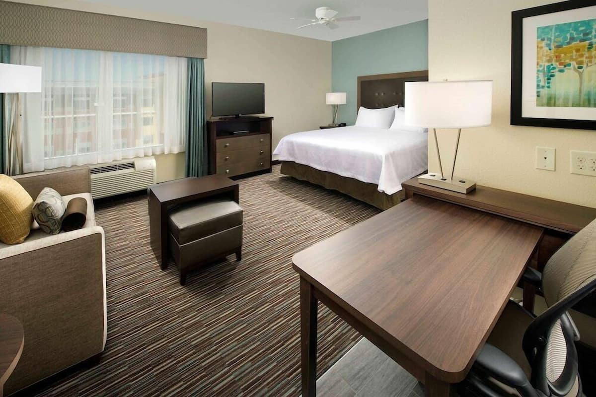 Une chambre d’hôtel avec un lit, un bureau, une chaise, une télévision et une fenêtre avec des rideaux.