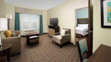 Una habitación de hotel con cama, televisor, sofá, sillón, escritorio y piso alfombrado.