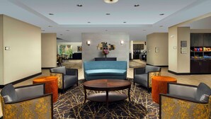 A lobby with a central seating area, a reception desk, and a kitchenette in the background.