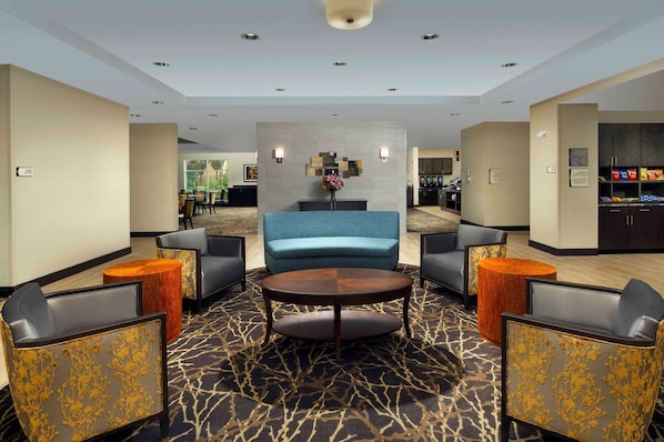 A lobby with a central seating area, a reception desk, and a kitchenette in the background.