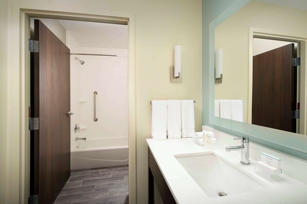 Un baño moderno con ducha, lavamanos con espejo y perchero para toallas.
