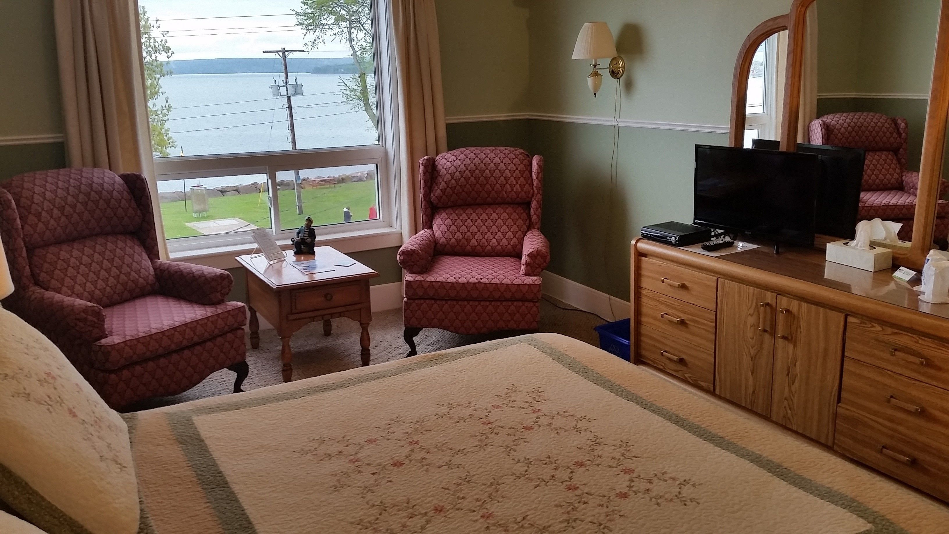 A hotel room with a bed, two armchairs, a small table, a television, and a dresser.