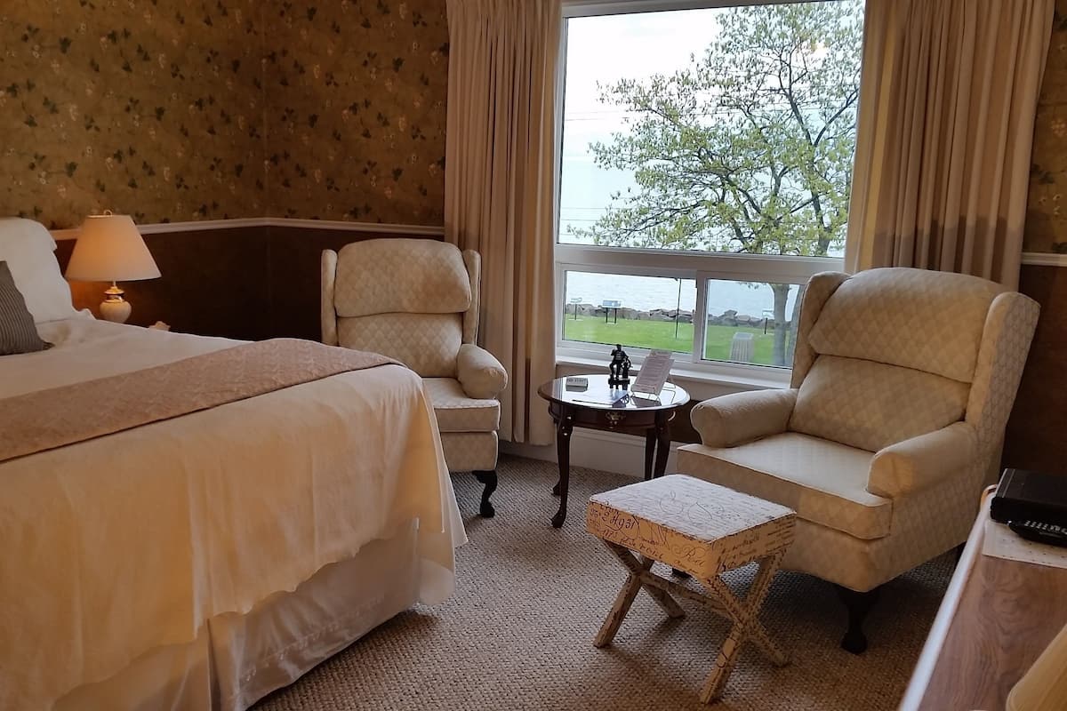 A hotel room with a bed, two armchairs, a small table, and a view of the outdoors.