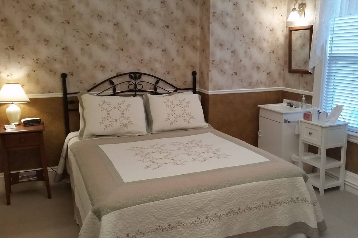 A neatly arranged bedroom with a bed, bedside table, lamp, and a small dresser.