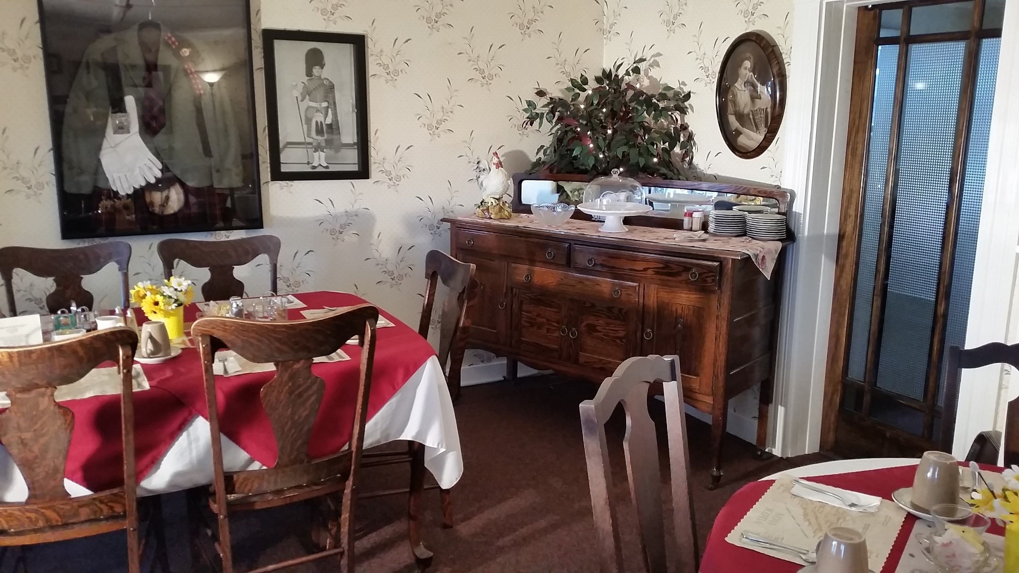A dining area with wooden chairs and tables, a wooden cabinet, and a red tablecloth.