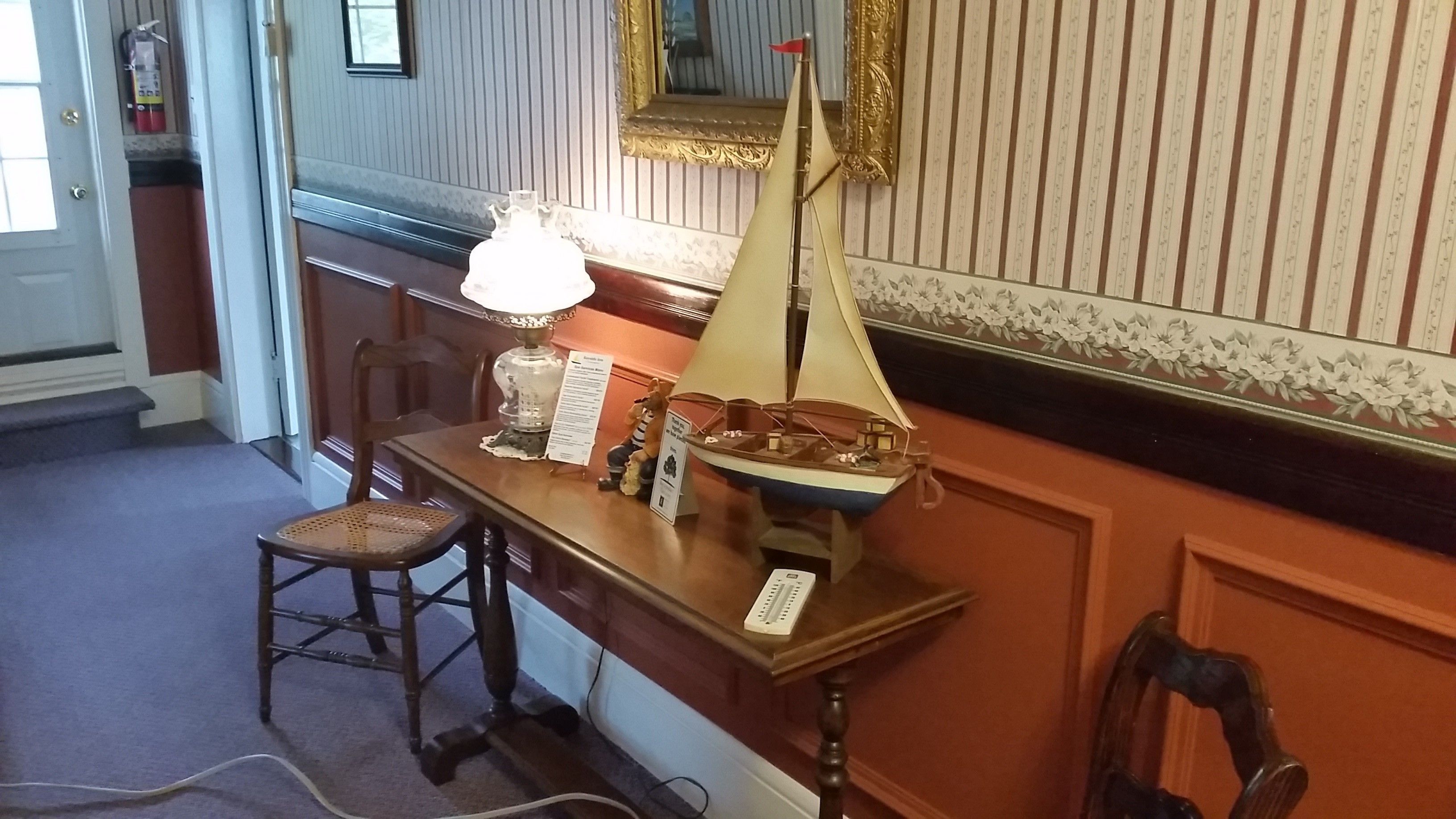 A room with a wooden table displaying a model ship, a lamp, and a small chair.