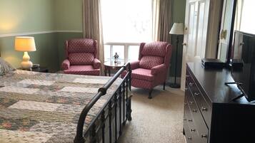 A hotel room with a bed, two armchairs, a dresser, a television, and a window with curtains.